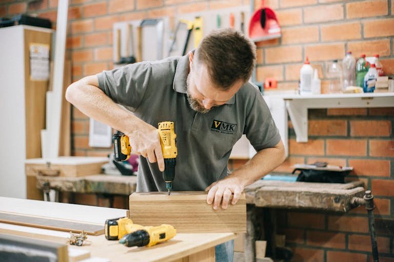 A carpenter working with a drill in a well-equipped workshop.